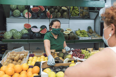 Ein Ladenbesitzer mit einer Maske bedient einen Kunden im Gemüseladen. - CAVF90409