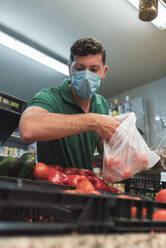 Ein Obstverkäufer mit einer Maske, der Obst aus einer Kiste nimmt - CAVF90410