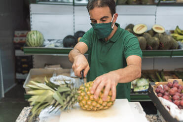 Ein Mann, der in seinem eigenen Obstladen eine Ananas schneidet. - CAVF90412