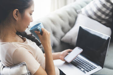 Frau, die am Laptop arbeitet und Kaffee trinkt. - CAVF90436