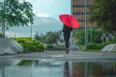 Frau mit rotem Regenschirm geht hinter einer Pfütze in Palma, Spanien - CAVF90568