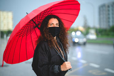 Porträt einer Frau mit einer Maske und einem roten Regenschirm, die in die Kamera schaut - CAVF90569