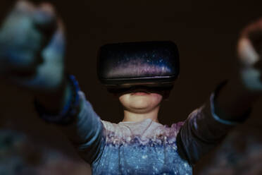 Süßer Junge mit VR-Brille, der unter einer bunten Projektion steht und virtuelle Realität erkundet - ADSF17186