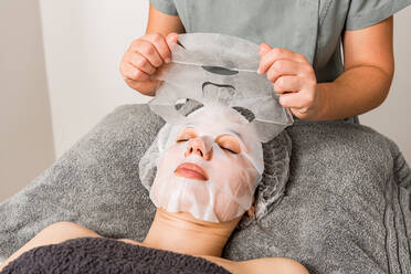 Anonyme Kosmetikerin, die während einer Verjüngungskur in einem modernen Schönheitssalon eine Gesichtsmaske auf die Kundin aufträgt - ADSF17192
