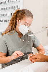Side view of young female specialist in protective mask doing professional manicure procedure in cropped unrecognizable male in modern beauty center - ADSF17201