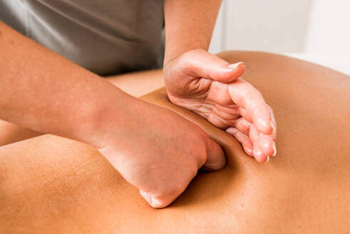 Abgeschnittene, nicht erkennbare weibliche Therapeutin, die in einer modernen Klinik eine Massage auf dem Rücken eines männlichen Klienten ausführt - ADSF17205