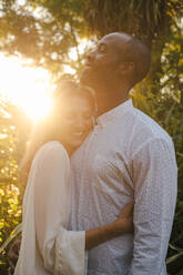 Loving multiracial couple in white shirts bonding and hugging tenderly while enjoying evening in summer garden in sunset time in Madrid Spain - ADSF17233