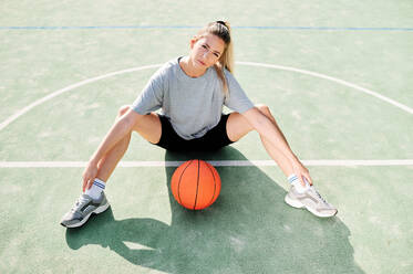 High angle view of young female basketball player sitting on court near ball - ADSF17262