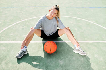 Hochwinkelaufnahme einer jungen Basketball-Spielerin, die auf dem Platz in Ballnähe sitzt - ADSF17262
