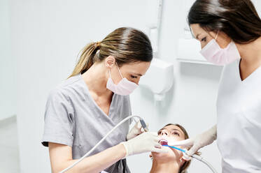 Female client in chair under bright lamp having teeth check up in modern dental clinic - ADSF17276