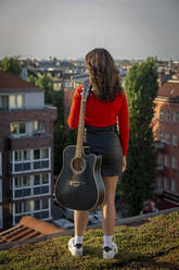 Junge Frau mit Gitarre auf dem Dach stehend - NGF00700