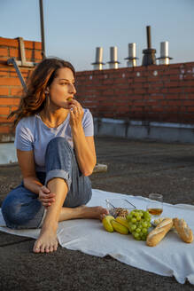 Young woman having fruits during picnic on rooftop - NGF00703