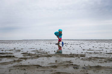 Mädchen spielt im Watt mit Schaufel gegen den Himmel im Nationalpark Niedersächsisches Wattenmeer, Deutschland - LHF00824