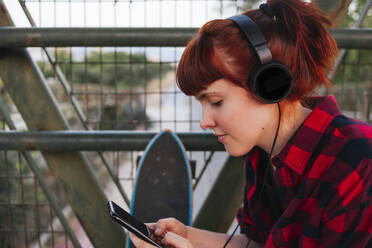 Redhead woman text messaging while listening music through headphones - MGRF00055