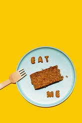 Slice of cake on blue plate with message Eat Me made of biscuit letters - GEMF04377