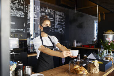 Kellnerin mit Gesichtsschutzmaske bei der Kaffeeausgabe in einem Cafe - BSZF01762