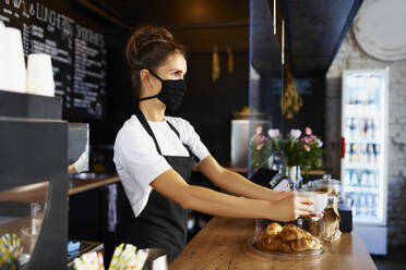 Weibliche Barista mit Gesichtsschutzmaske, die Kaffee ausschenkt, während sie in einem Café arbeitet - BSZF01764