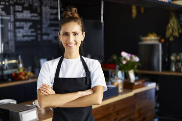 Portrait of smiling waitress with arms crossed working at cafe - BSZF01767