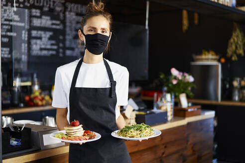 Porträt einer Barista mit Schutzmaske beim Servieren von Speisen in einem Café - BSZF01773