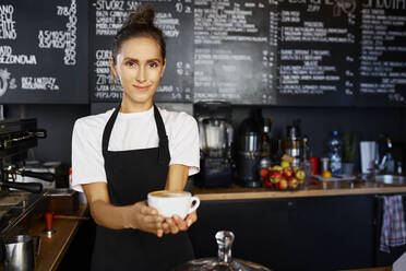 Portrait of smiling waitress giving coffee at cafe - BSZF01780