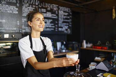 Lächelnde weibliche Barista, die in einem Café Kaffee ausschenkt - BSZF01781