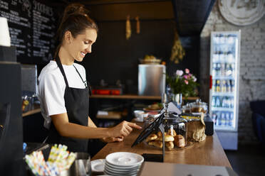 Smiling barista using digital tablet at kitchen counter in cafe - BSZF01785