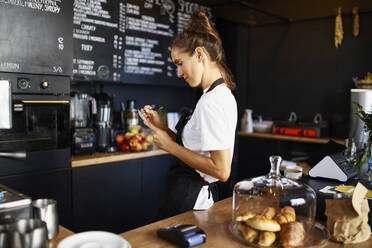 Barista schreibt in Notizblock bei der Arbeit im Café - BSZF01787