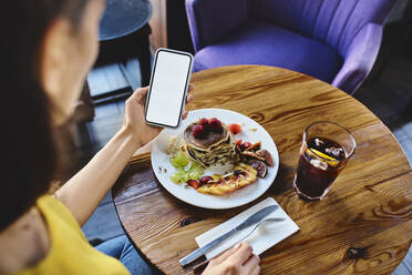 Hohe Winkel Ansicht der jungen Frau mit Pfannkuchen mit Smartphone am Tisch im Café - BSZF01800