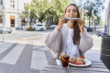 Frau, die ein Foto von Essen und Getränken auf dem Tisch macht, während sie auf dem Bürgersteig in einem Café sitzt - BSZF01805