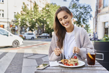 Woman smiling while eating food and drink at sidewalk cafe - BSZF01807