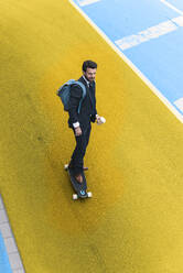 Young businessman skateboarding on yellow and blue street - UUF22058