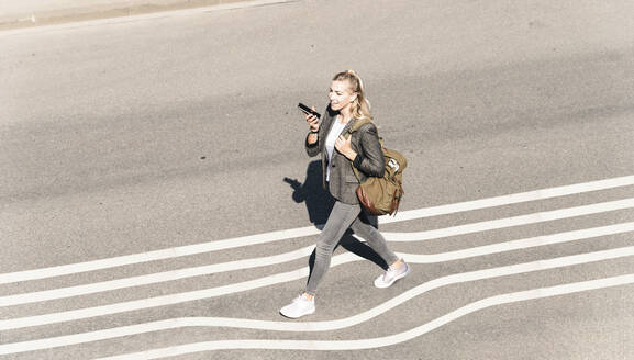 Junge Frau spricht mit ihrem Smartphone, während sie an einem sonnigen Tag auf der Straße geht - UUF22062