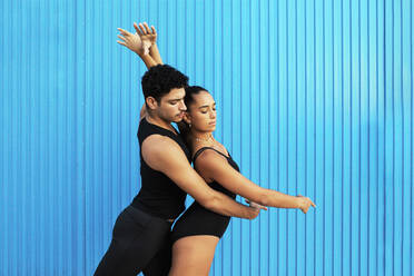 Young male and female gymnasts doing dancing pose by blue wall - MIMFF00259