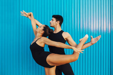 Young male gymnast assisting female dancer balancing by blue wall - MIMFF00261