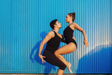 Professional gymnast couple doing balancing pose by blue corrugated metal - MIMFF00263