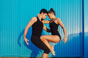 Male and female professional gymnasts doing balancing pose by blue corrugated metal - MIMFF00264