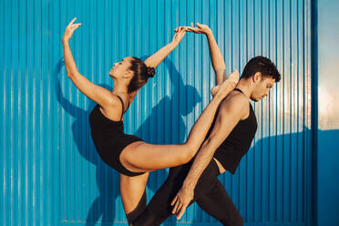 Professional gymnast couple doing attitude balance pose by blue wall - MIMFF00266