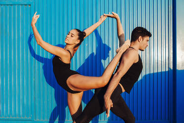 Male and female professional gymnast couple doing attitude balance pose by blue wall - MIMFF00267
