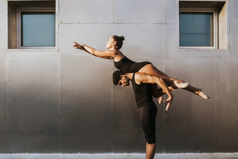 Male gymnast carrying female on shoulders while practicing dance posture by wall stock photo