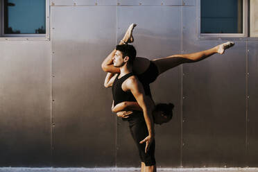 Professional male gymnast holding female upside down while doing dance posture by wall - MIMFF00274