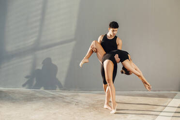 Professioneller männlicher Tänzer hilft einer Turnerin in Tanzpose gegen die Wand - MIMFF00276
