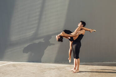 Young man helps flexible woman do dance pose against wall - MIMFF00277