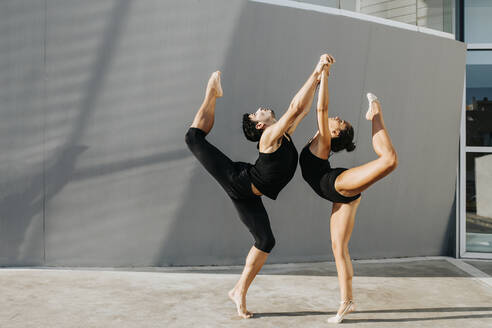 Professional gymnasts standing on one leg while balancing by gray wall - MIMFF00278