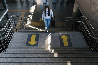 Frau mit Gepäck auf der Treppe eines Bahnhofs während einer Pandemie - EGAF00986