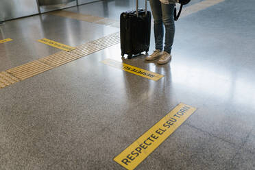 Woman with luggage waiting her turn by sign on flooring at subway station - EGAF00988