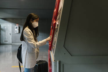 Woman with face mask using kiosk for buying train ticket during COVID-19 - EGAF00990