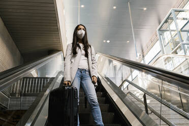 Woman wearing face mask while standing with luggage on escalator at subway station - EGAF00992