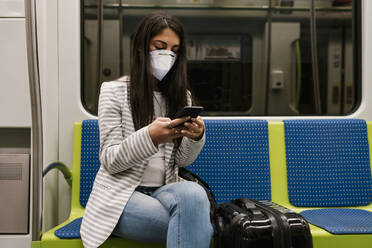 Female passenger using smart phone while sitting in metro train - EGAF00993