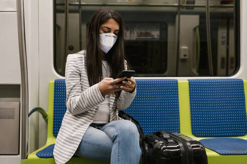 Weiblicher Fahrgast, der im U-Bahn-Zug sitzend sein Smartphone benutzt - EGAF00993