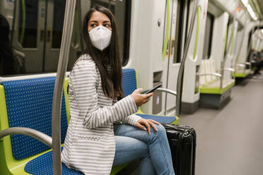 Woman looking away while sitting with smart phone in metro train - EGAF00994